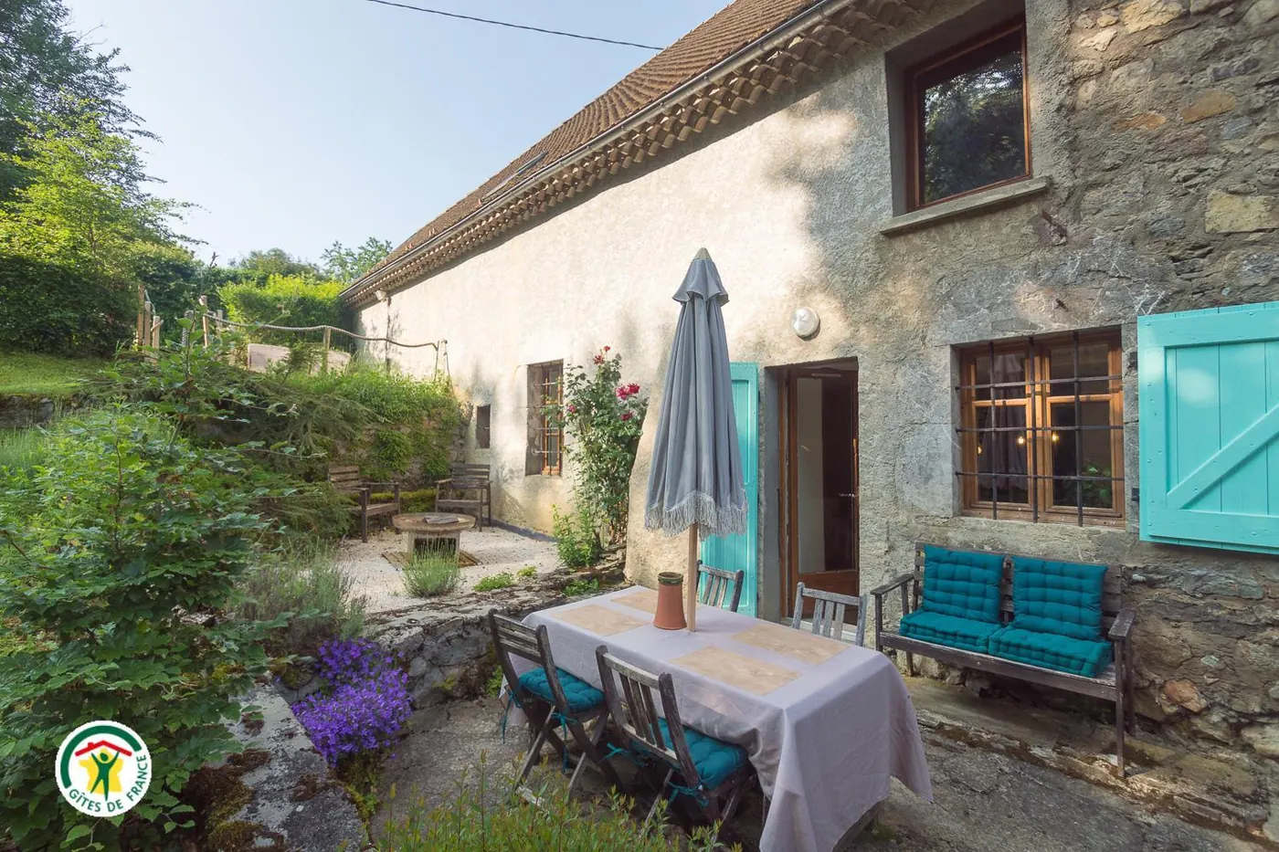 La terrasse du Gîte du Lys et sa façade en pierre aux volets turquoise, un soir d'été